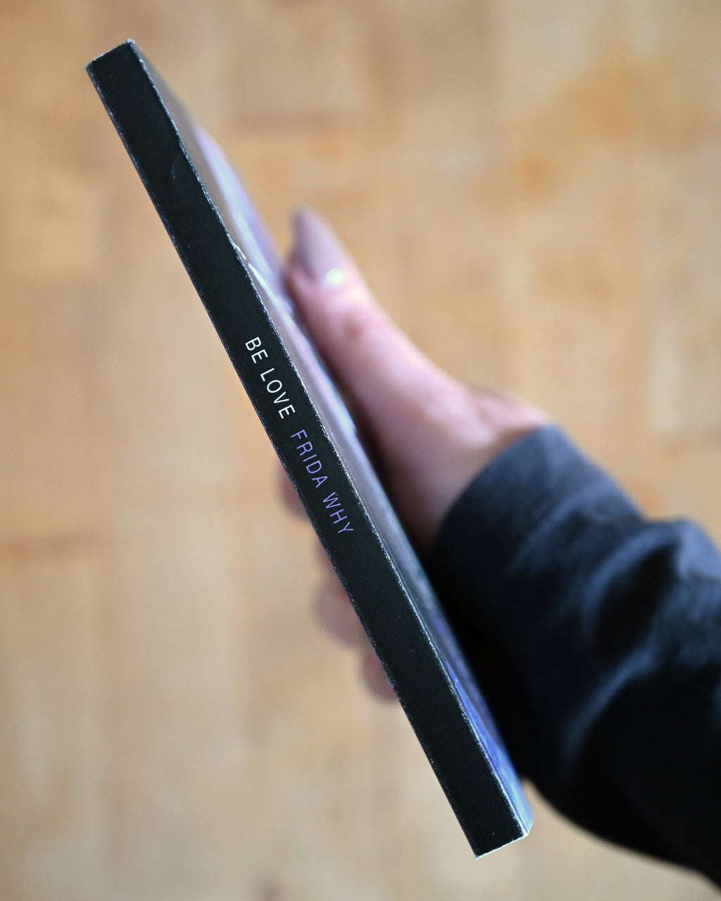Hand holding a black and clear cosmetic product with text on a wooden surface