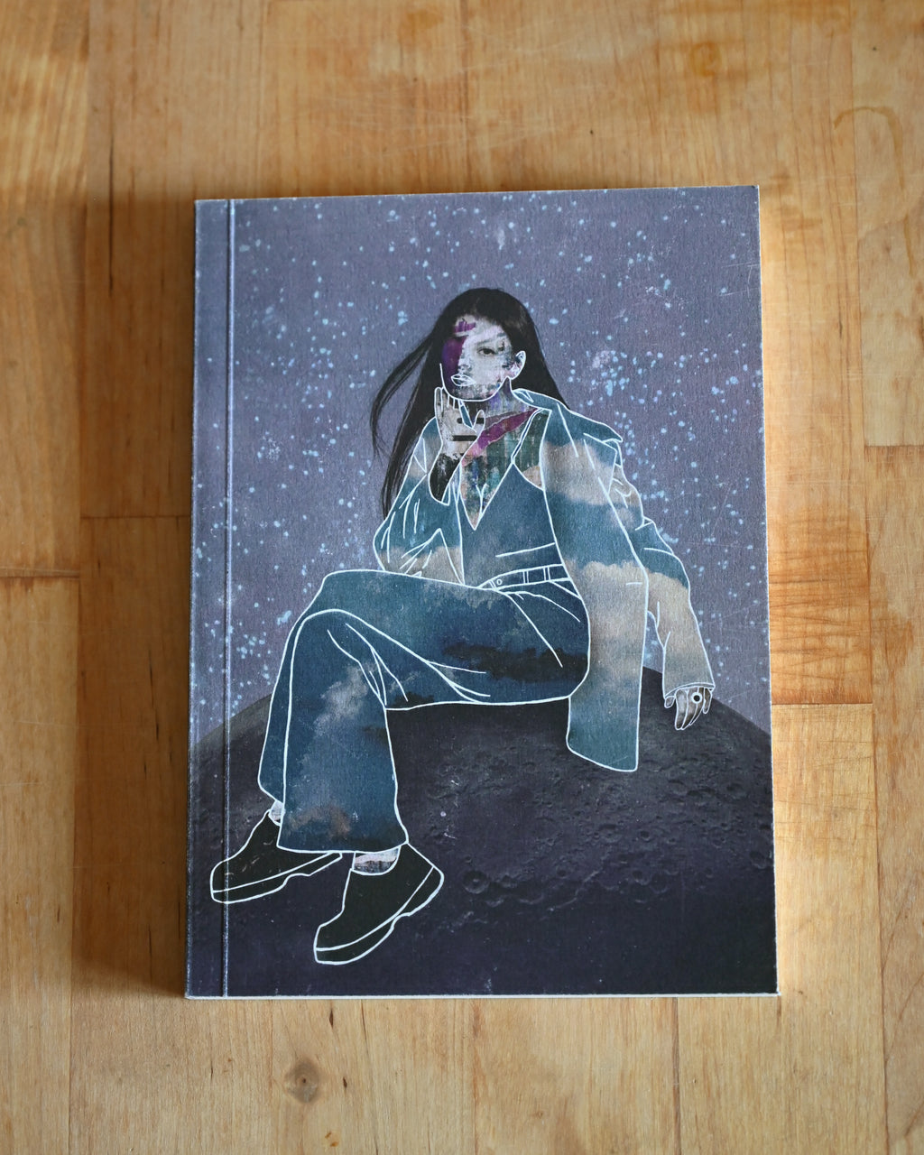 Illustrated notebook with a person on the moon sitting on a wooden surface