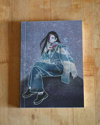 Illustrated notebook with a person on the moon sitting on a wooden surface