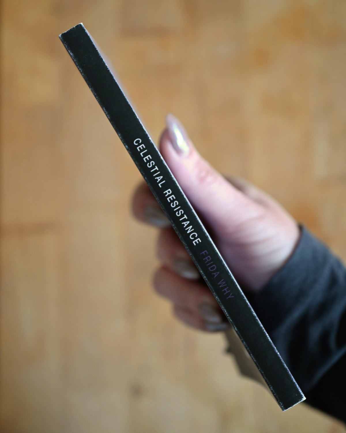 Hand holding a black cosmetic pencil labeled 'Celestial Resistance' on a wooden surface.