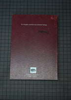 A dark red sketchbook or notebook with white text reading 'For thoughts, sketches and unfinished feelings.' and a small eye logo near the bottom, placed on a dark gridded surface.