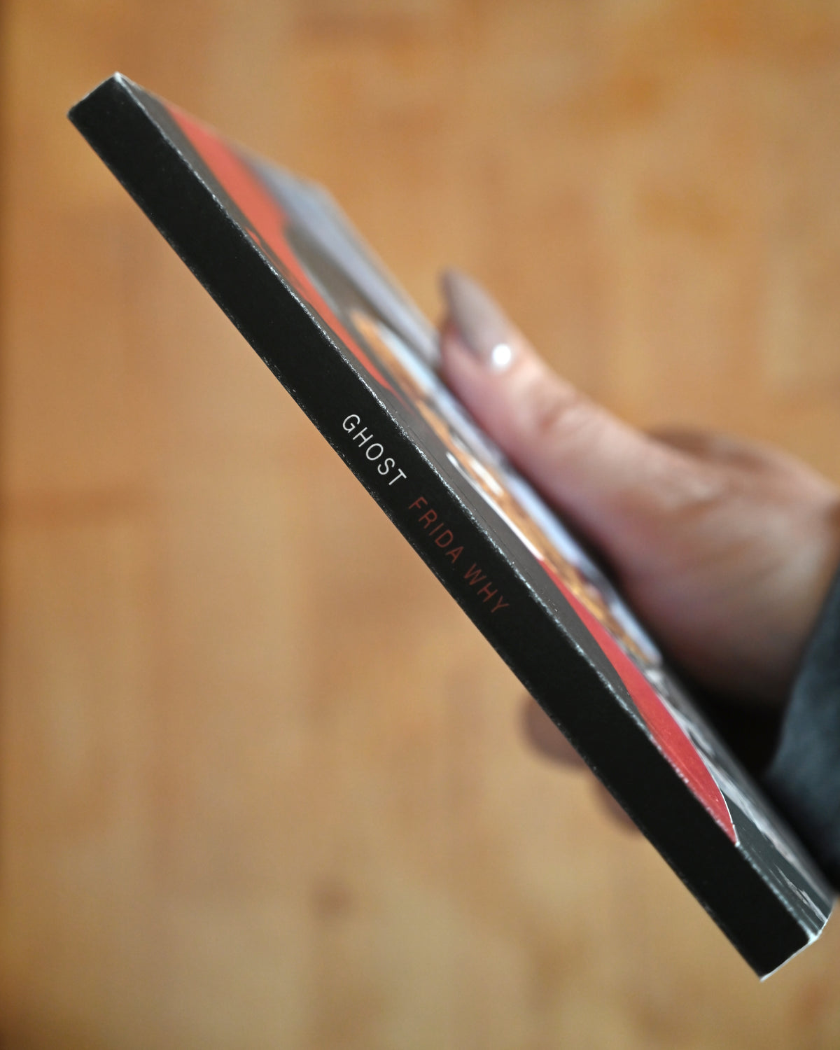 Hand holding a product with 'Ghost' branding against a wooden background