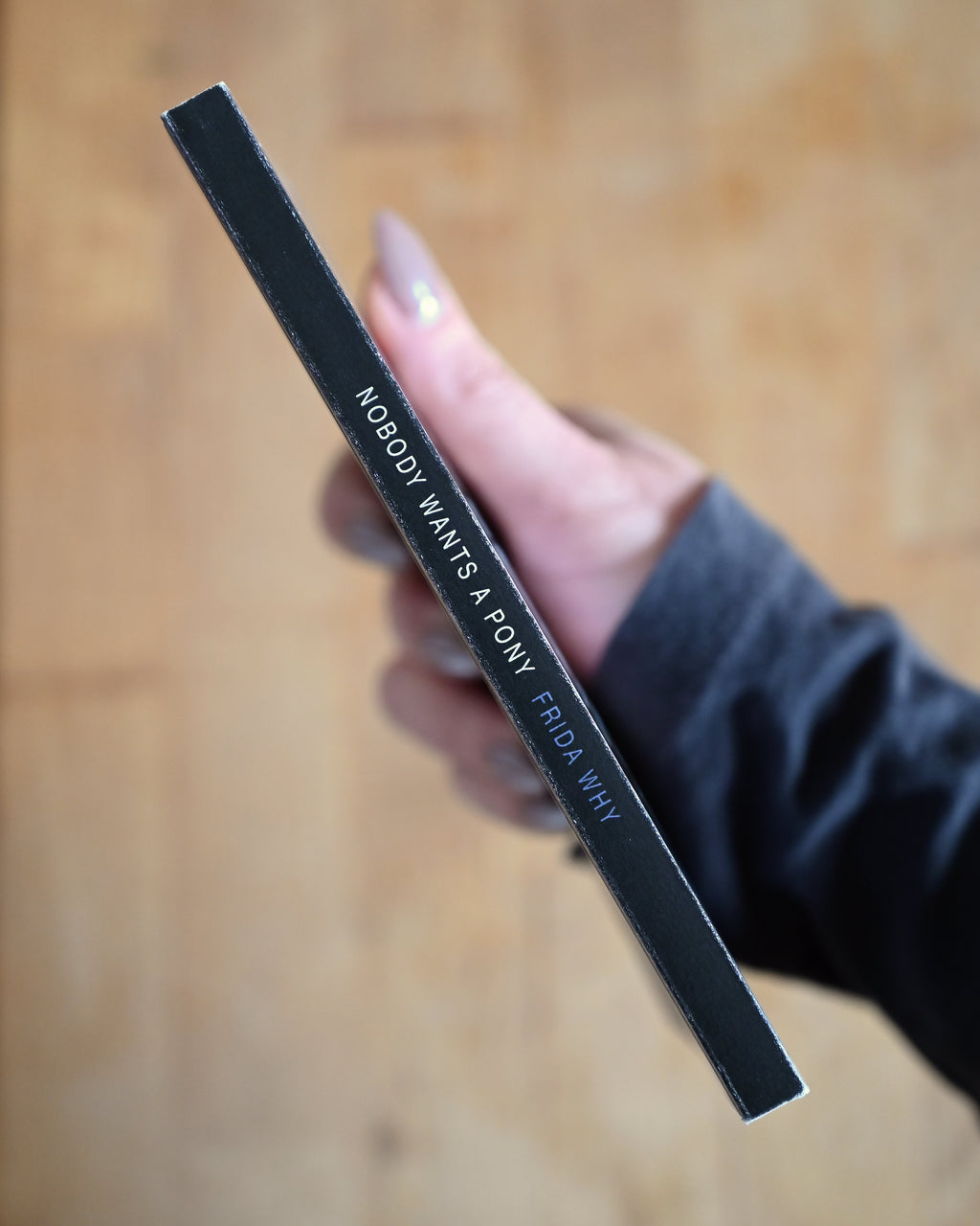 Black pen with text held by a hand on a wooden surface