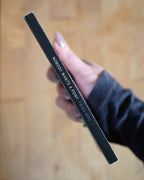Black pen with text held by a hand on a wooden surface