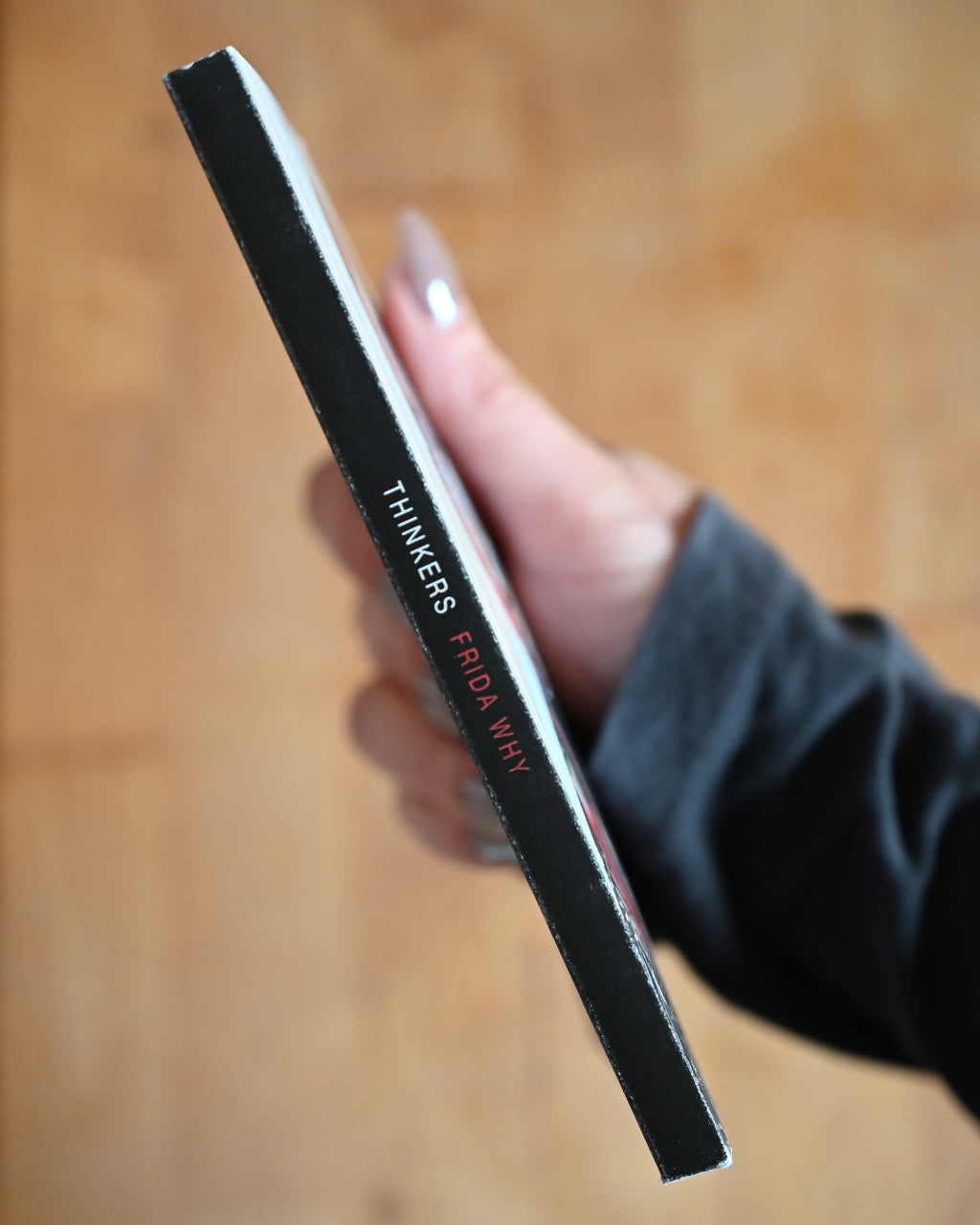 Hand holding a black rectangular object with 'THINKERS' branding on a wooden surface