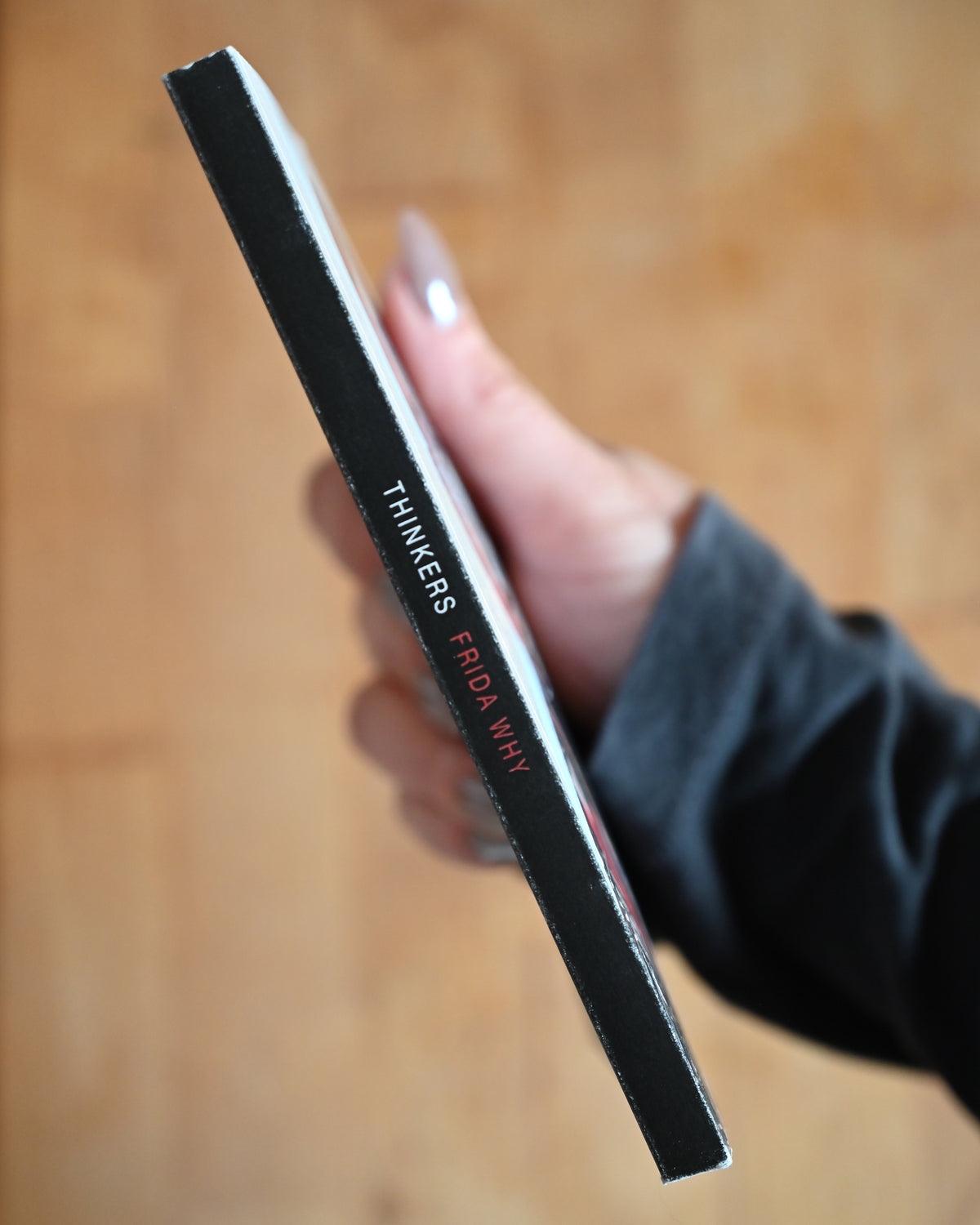 Hand holding a black rectangular object with 'THINKERS' branding on a wooden surface