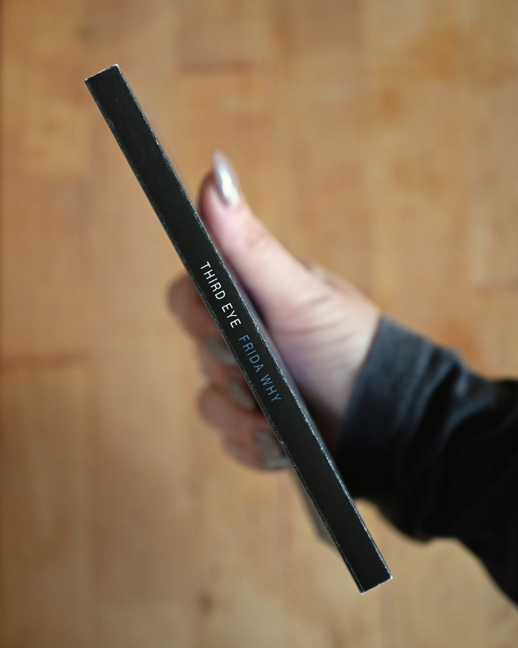 Black eyeliner pencil held by a hand on a wooden surface
