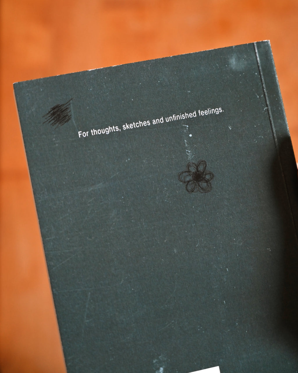 Black notebook with text and a flower drawing on an orange background