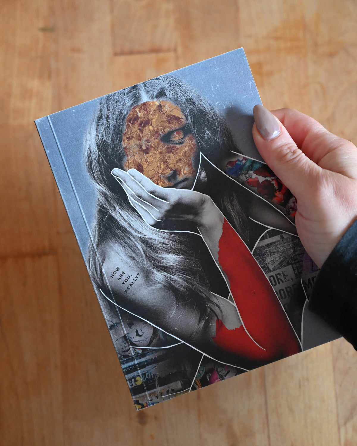 Book with a cover featuring an artistic illustration of a woman holding a child, held by a hand on a wooden surface.