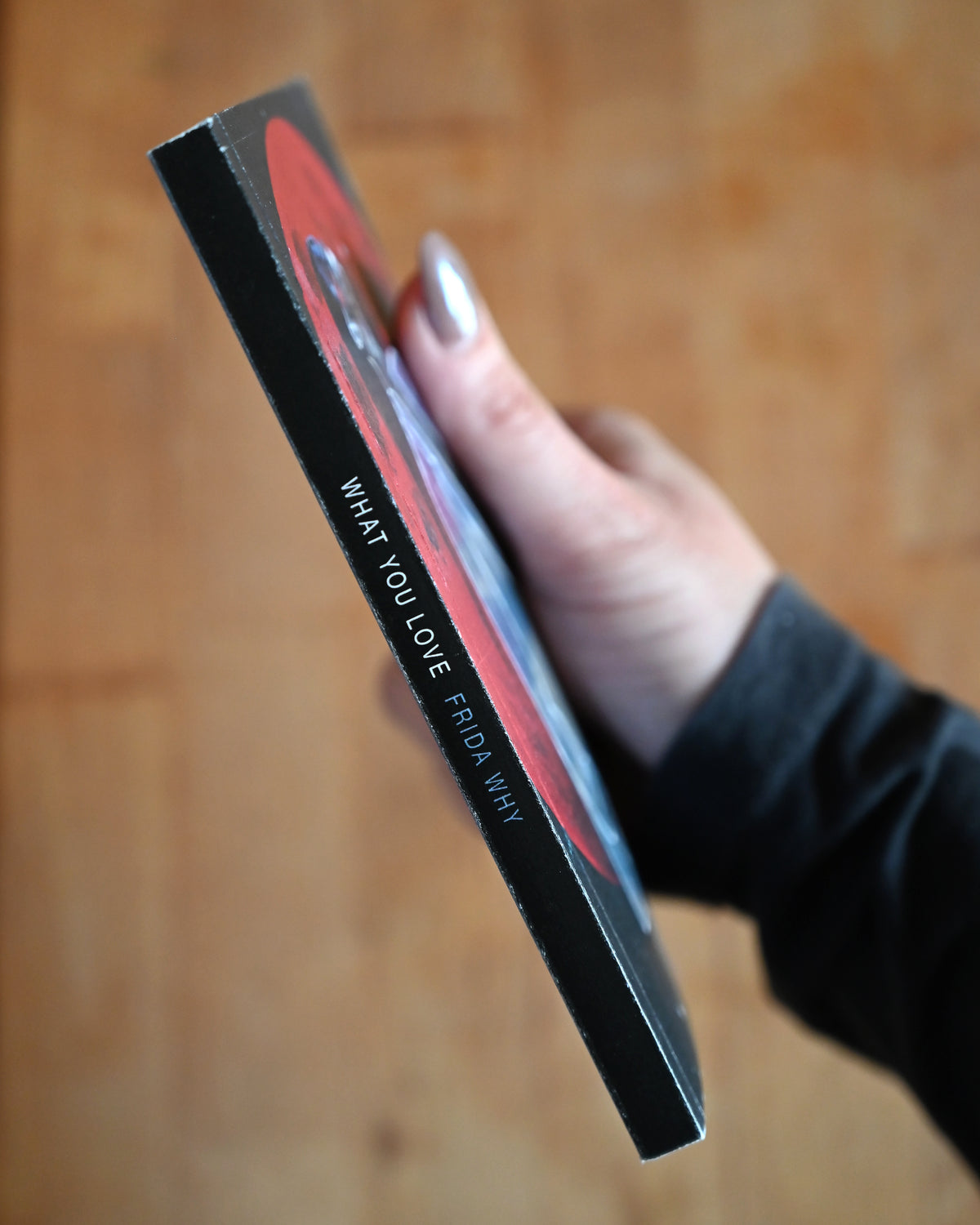 Hand holding a product packaging with 'What You Love Frida' text on a wooden surface