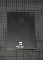A black sketchbook or notebook with white text and a small logo near the bottom, placed on a dark grid-patterned surface.