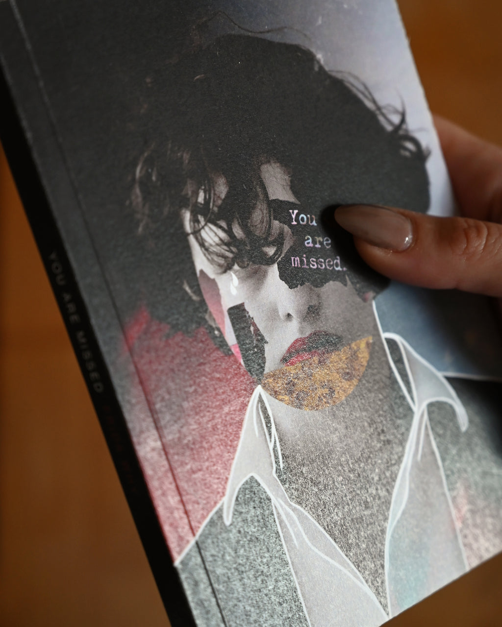 Book cover with artistic design and text 'You are missed' held by a hand.