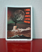 A rectangular art print or card with a white border, featuring a dark tree in front of a large moon over snowy mountains, with red text reading 'I WISH SOME NIGHTS LASTED FOREVER.' It is photographed standing on a glossy red surface against a light gray wall.