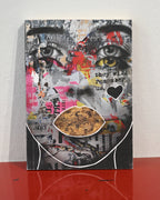 A mixed-media collage art print featuring a stylized face with cutout eyes and lips, displayed on a red reflective surface against a white wall.