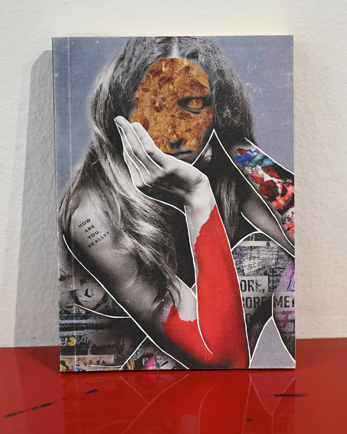 A square canvas art print featuring a surreal collage of a woman with long dark hair, a pizza slice for a face, and bold red and black graphic elements, displayed standing on a glossy red surface against a white wall.