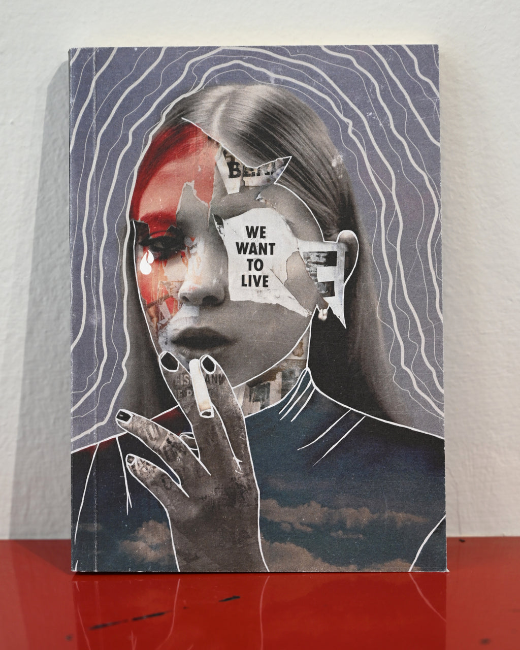 A square canvas art print featuring a surreal collage portrait of a woman with red, white, and black elements, set against a gray background with white wavy lines. The print is displayed standing on a red reflective surface against a white wall.